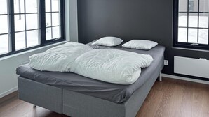 A modern bedroom with a grey sofa bed, white pillows, and large windows offering a view of the outdoors. - Stunning apartment in Idre with sauna (Idre)