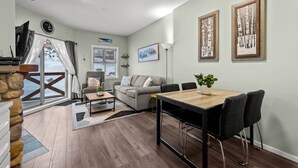 Een moderne woonkamer met een houten eettafel, zwarte stoelen, een grijze bank en een groot raam met uitzicht op de omgeving.