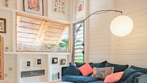 A cozy living room with a teal sofa, a round coffee table, and a large window with wooden beams.