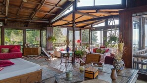 A spacious room with a wooden ceiling, large windows, and a view of greenery outside.