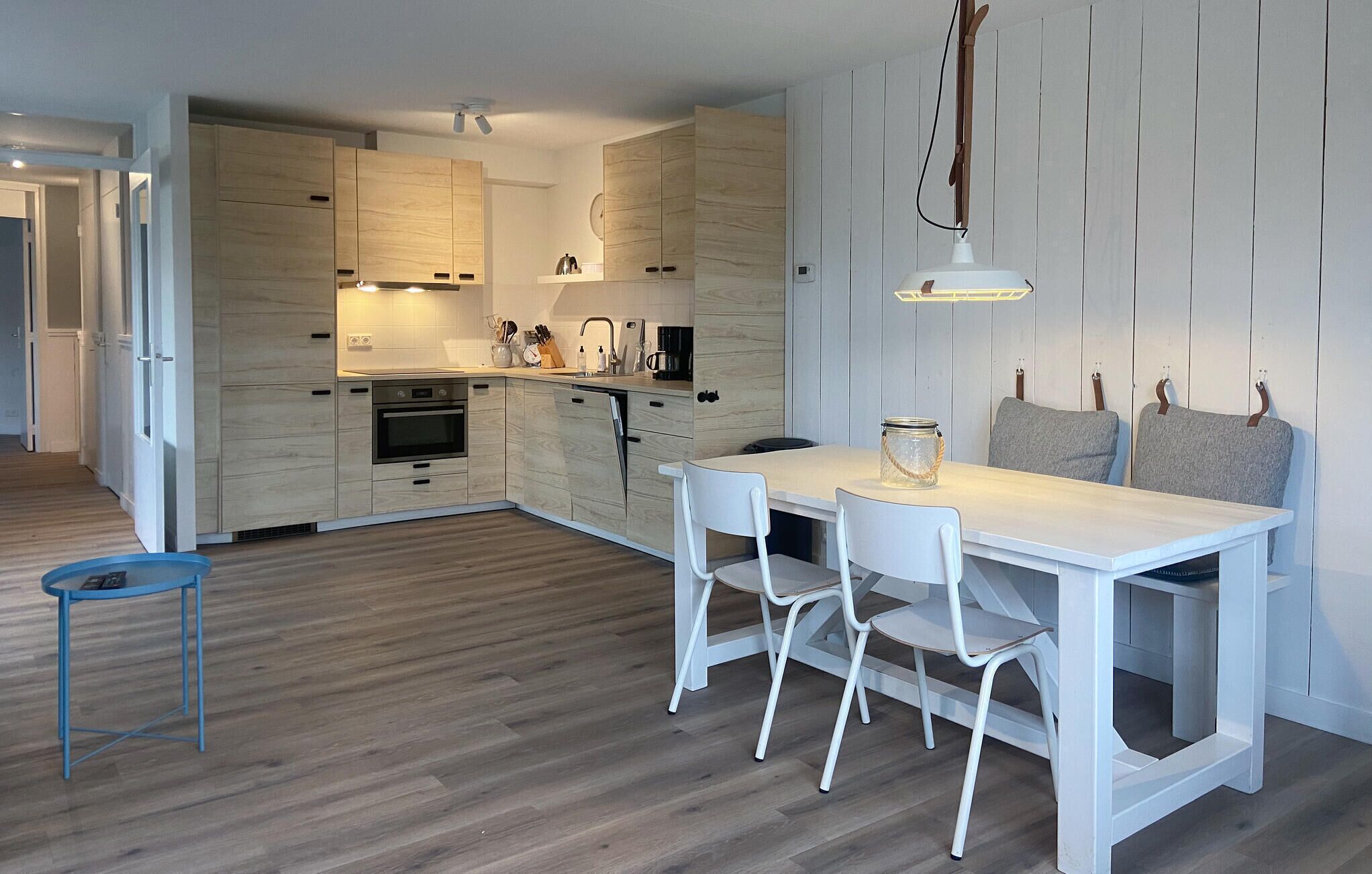 Une cuisine moderne avec des meubles en bois, un îlot central et un coin repas comprenant une table et des chaises blanches.
