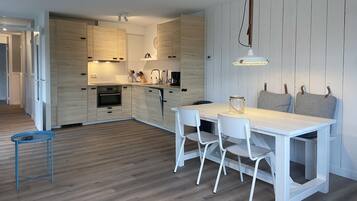 Une cuisine moderne avec des meubles en bois, un îlot central et un coin repas comprenant une table et des chaises blanches.
