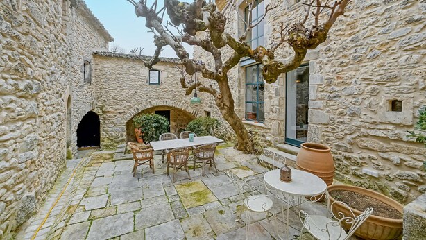 Ein steinerner Innenhof mit Tisch und Stühlen, einem großen Baum und Kübelpflanzen.