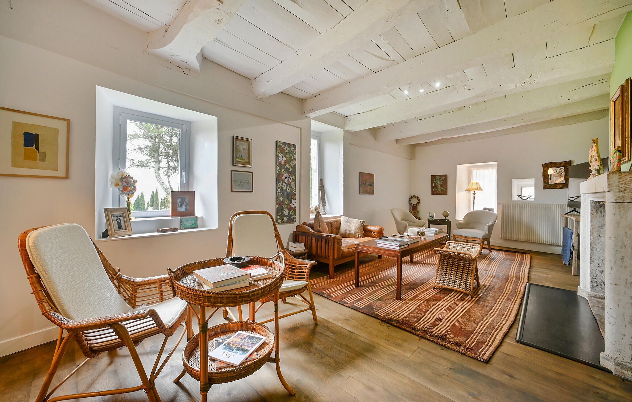 Un salon spacieux avec un plafond haut, des meubles en osier et une grande fenêtre qui laisse entrer la lumière naturelle.