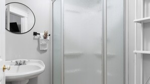 Casa de banho com lavatório branco, espelho e cabine de duche em vidro.