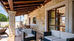 A covered outdoor seating area with stone walls, wicker furniture, and a view of the surrounding landscape. - Stunning home in Valtura (Valtura)