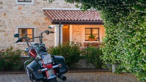 A motorcycle parked in front of a stone building with a tiled roof and a garden with flowering plants. - Stunning home in Valtura (Valtura)