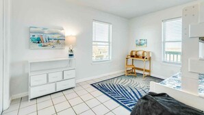 Una habitación con un aparador blanco, un tapete azul y blanco, una silla de madera y una cama con colcha estampada.
