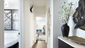 A hallway with a bed, a black vase with white flowers, and a modern abstract wall art piece.