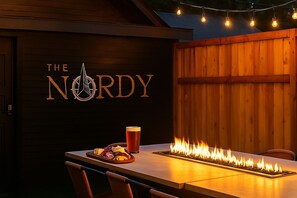 Ett träbord med en inbyggd eldstad, ett glas öl och en tallrik mat. På väggen finns en logotyp med texten ”THE NORDY”.