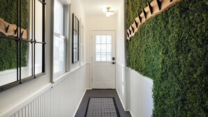 A hallway with a white door, a black and white patterned rug, and a green wall covered with foliage.