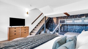 Um quarto com uma cama beliche, uma televisão de tela plana, um aparador de madeira e uma escada.