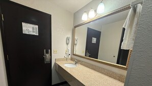 A bathroom with a dark door, a sink, a mirror with lights, and a towel hanging on the wall. - Red Roof PLUS+ Centralia (Centralia)