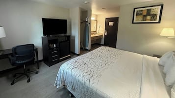 Habitación de hotel con cama, escritorio y silla, televisor, baño con espejo y un cuadro en la pared.