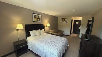 Une chambre d’hôtel comprenant un lit, des tables de chevet, une lampe, une chaise, une commode et un miroir.