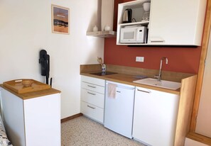 Eine kompakte Küche mit weißen Schränken, einer Holz Arbeitsplatte, einer Mikrowelle und einem Spülbecken.