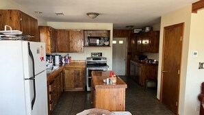 Una cocina con gabinetes de madera, un refrigerador, un horno, un microondas e una isla de madera con hielera.