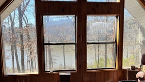 Un dormitorio con ventanas amplias, una cama y vistas a árboles y un lago.