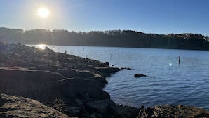 Una costa rocosa con un lago tranquilo, cielo despejado y árboles a lo lejos.