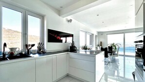 A modern kitchen with large windows, a dining area, and a view of the sea.