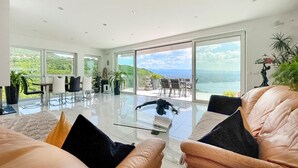 A spacious living room with a glass coffee table, leather sofas, and a view of a mountainous landscape through large windows.
