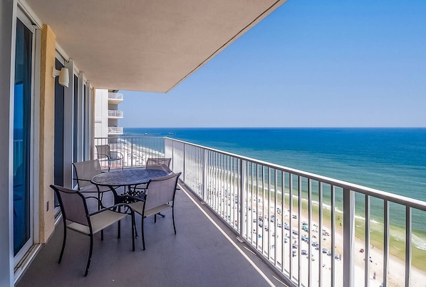 A balcony with a table and chairs, overlooking a beach and the ocean.