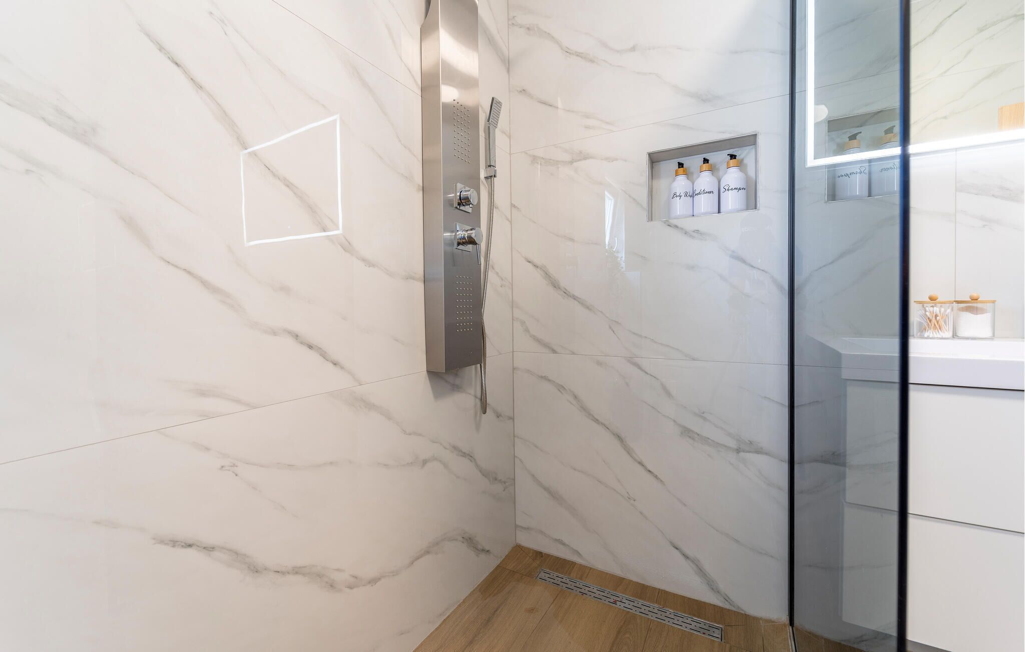 Un baño moderno con paredes de mármol, ducha y mampara de vidrio.