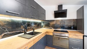 Une cuisine moderne avec des meubles de couleur sombre, un pare-feu en marbre et des appareils électroménagers en acier inoxydable.