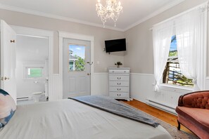 A bedroom with a large bed, a dresser, a television, and a window with curtains.