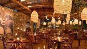 Ein Restaurant mit Holztischen und -stühlen, hängenden Lampen und einem Wandgemälde.