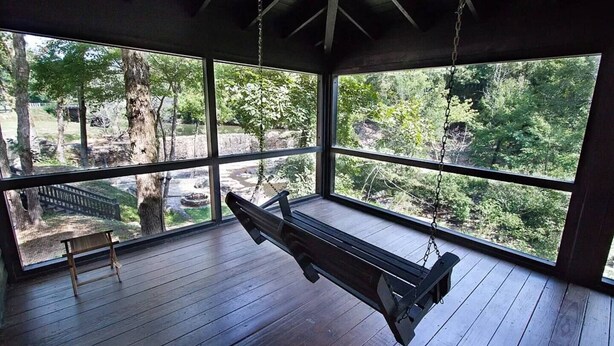 Un terrazzo in legno con un'altalena, ampie finestre e una panchina.