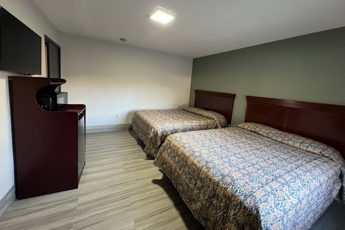 A hotel room with two beds, a desk with a flat-screen TV, and a ceiling light.