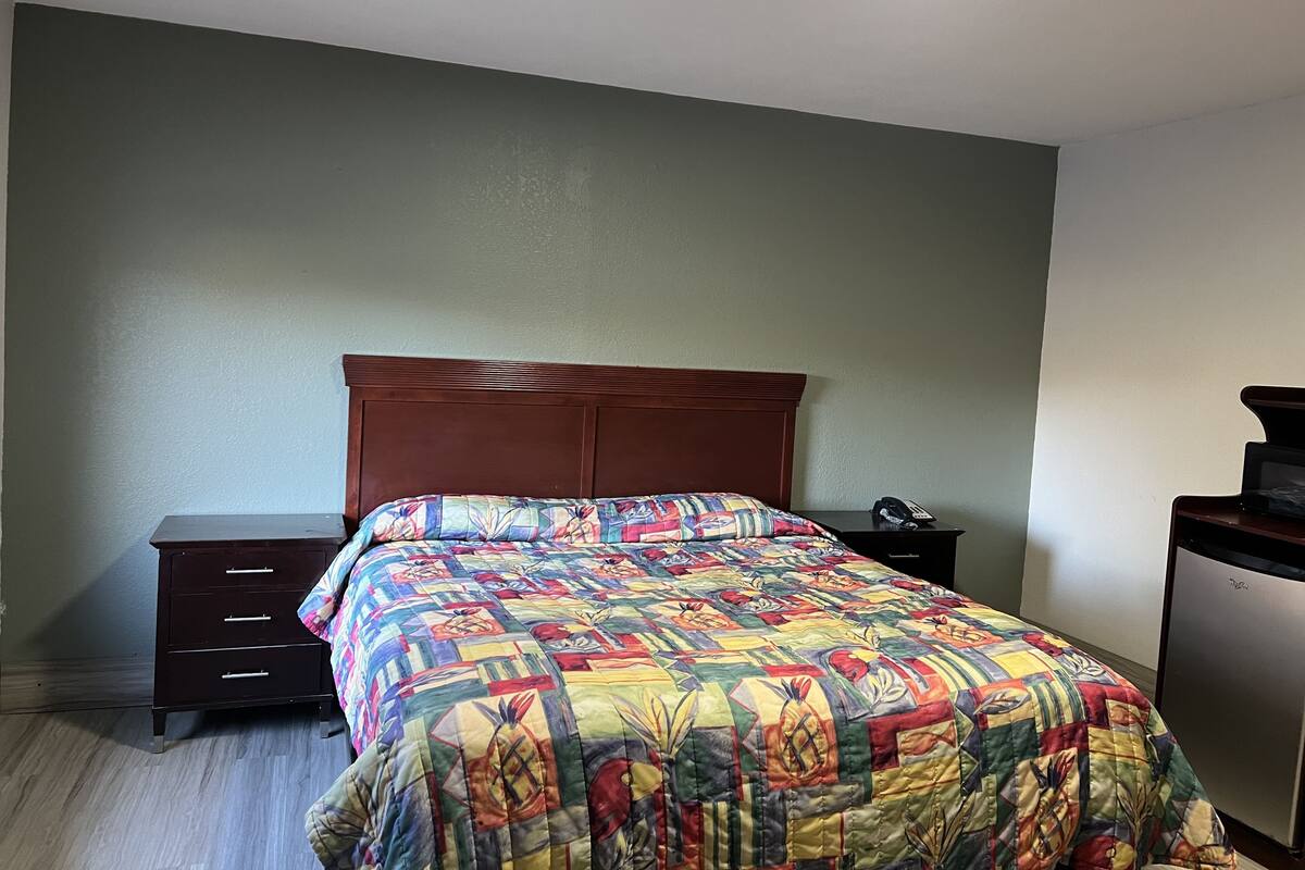 A bedroom with a wooden headboard, a colorful quilt, a small bedside table with a phone, and a dresser.