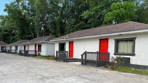 A row of single-story mobile homes with red doors and black railings, set against a backdrop of trees. - La Familia Stay Inn (Quincy)
