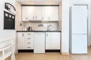 Una cocina compacta con armarios blancos, lavavajillas, refrigerador y un reloj de pared.