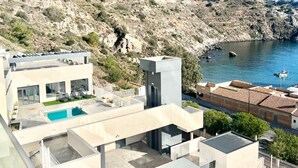 A modern building with a swimming pool, a view of the sea, and a rocky hillside in the background. - Apartment 'Icon Marina B' with Sea View, Wi-Fi and Air Conditioning (La Herradura)