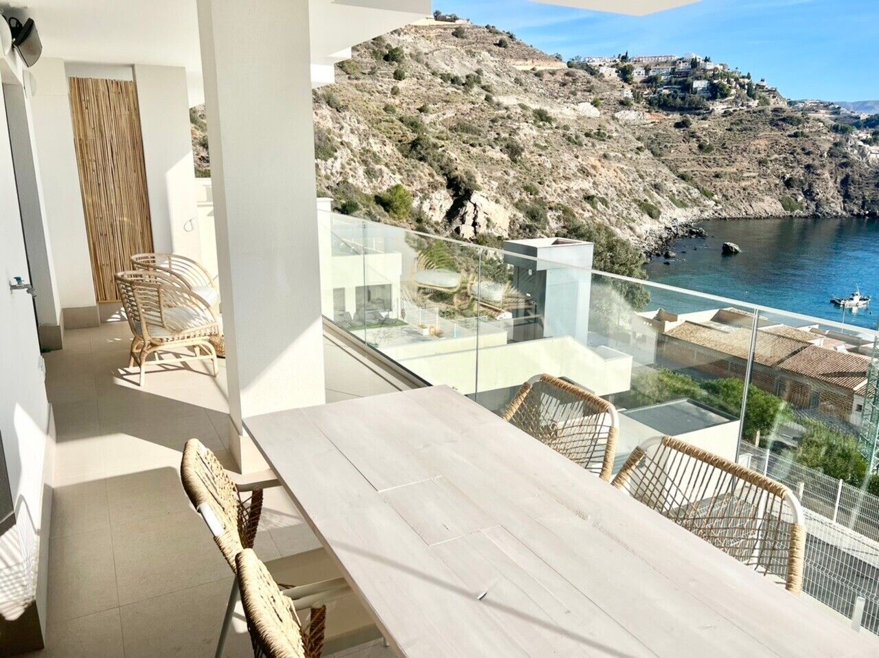 Een balkon met een tafel en stoelen, met uitzicht op een rotsachtige kustlijn met gebouwen.