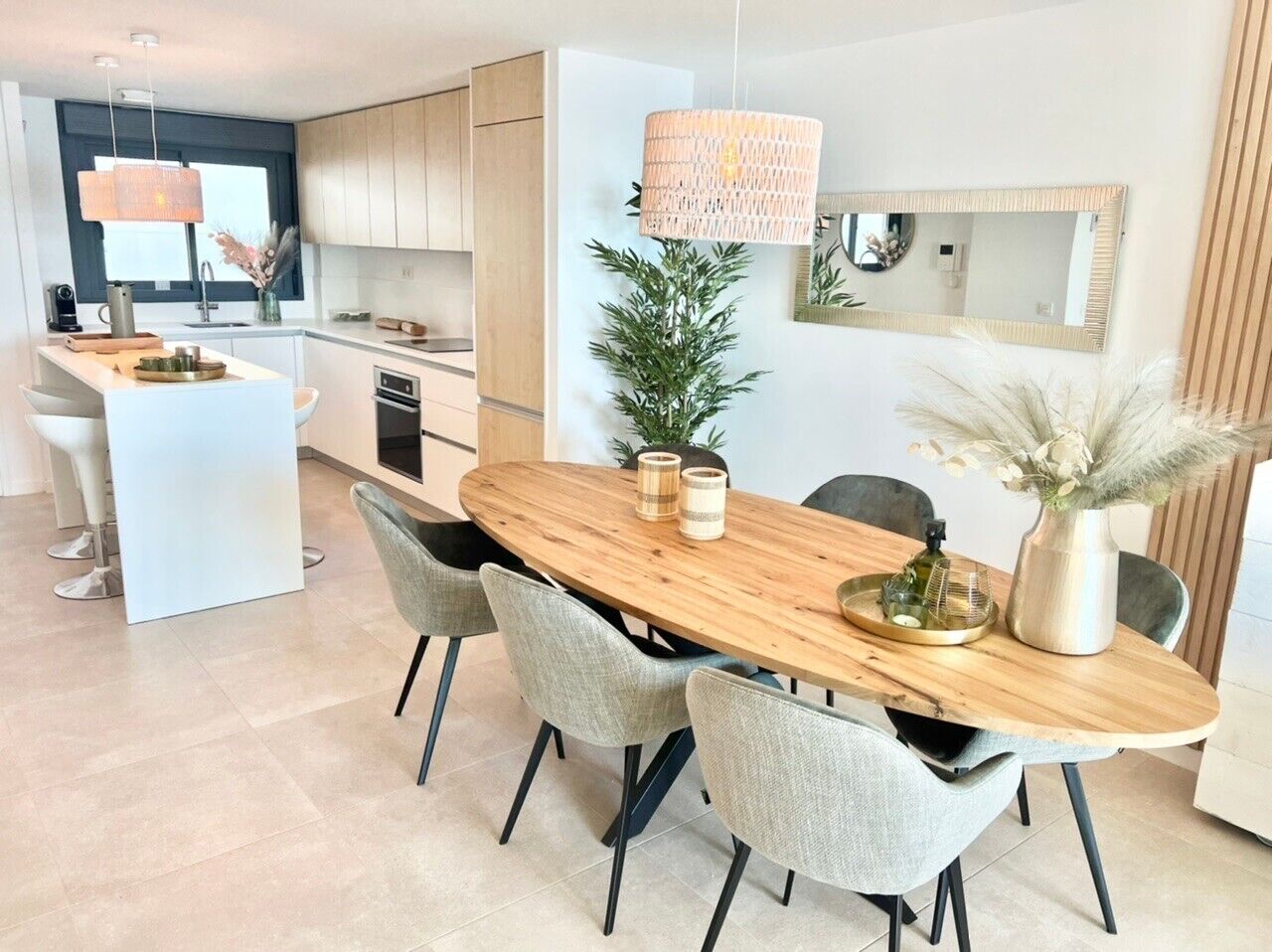 A modern kitchen with white cabinets, a central island, and a dining area with a wooden table and grey chairs.