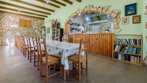 A dining area with a stone wall, wooden ceiling beams, a stone archway, and a bookshelf. - Holiday Home 'La Xaconera' with Private Pool, Wi-Fi and Air Conditioning (Riera de Gaia)