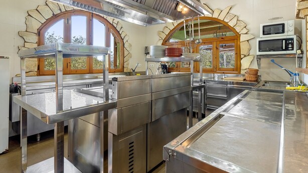 A commercial kitchen with stainless steel appliances, a stone arch window, and a microwave. - Holiday Home 'La Xaconera' with Private Pool, Wi-Fi and Air Conditioning (Riera de Gaia)