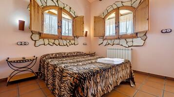 Ein Schlafzimmer mit Bett, zwei Fenstern mit Holzrollläden, einem Heizkörper und einem kleinen Tisch.