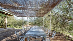 A covered outdoor dining area with a long table and metal chairs. - Holiday Home 'La Xaconera' with Private Pool, Wi-Fi and Air Conditioning (Riera de Gaia)