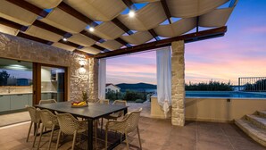 Eine Terrasse im Freien mit Tisch und Stühlen, einer Steinmauer und Blick auf ein Gewässer bei Sonnenuntergang.
