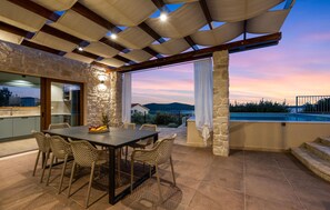 Enjoy meals al fresco with a dining table set for four, surrounded by wicker chairs and a pergola with a canopy.