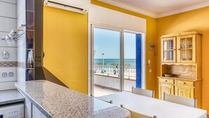 A kitchen with a granite countertop, a dining table, and a view of the beach through a glass door. - Apartment 'Mimosa' with Sea View, Wi-Fi and Air Conditioning (L'Escala)