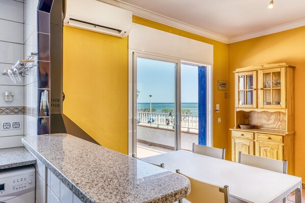 A kitchen with a granite countertop, a dining table, and a view of the beach through a glass door. - Apartment 'Mimosa' with Sea View, Wi-Fi and Air Conditioning (L'Escala)