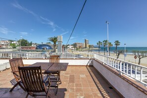 A terrace with a table and chairs, overlooking a beach and buildings.