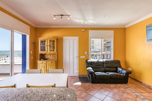 A room with a dining table, a leather sofa, a cabinet, and a door leading to a balcony.