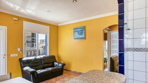 A room with a yellow wall, a black leather sofa, a white table, and a tiled floor. - Apartment 'Mimosa' with Sea View, Wi-Fi and Air Conditioning (L'Escala)