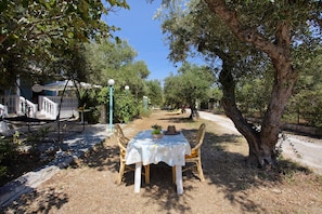 Zona pranzo all'aperto con tavolo e sedie, circondata da alberi e un vialetto.